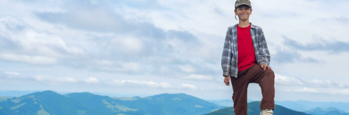 Un garçon au sommet d'une montagne devant un beau panorama.