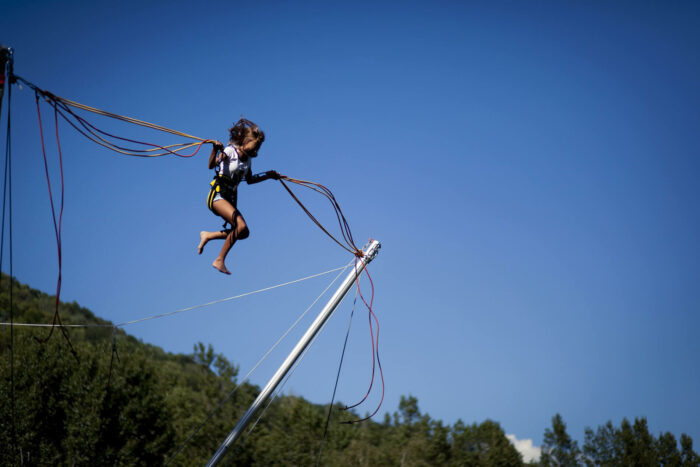 Jeune fille accrochées à des élastiques sautant sur un trampoline à la Base des Loisirs des Versants d'Aime.