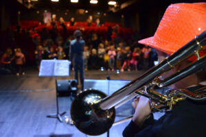 Garçon de dos jouant du trombone face à un public.