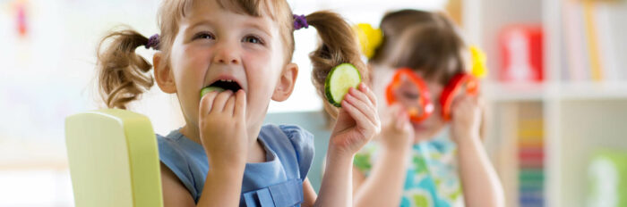 Deux enfants jouent avec des légumes et les mangent.